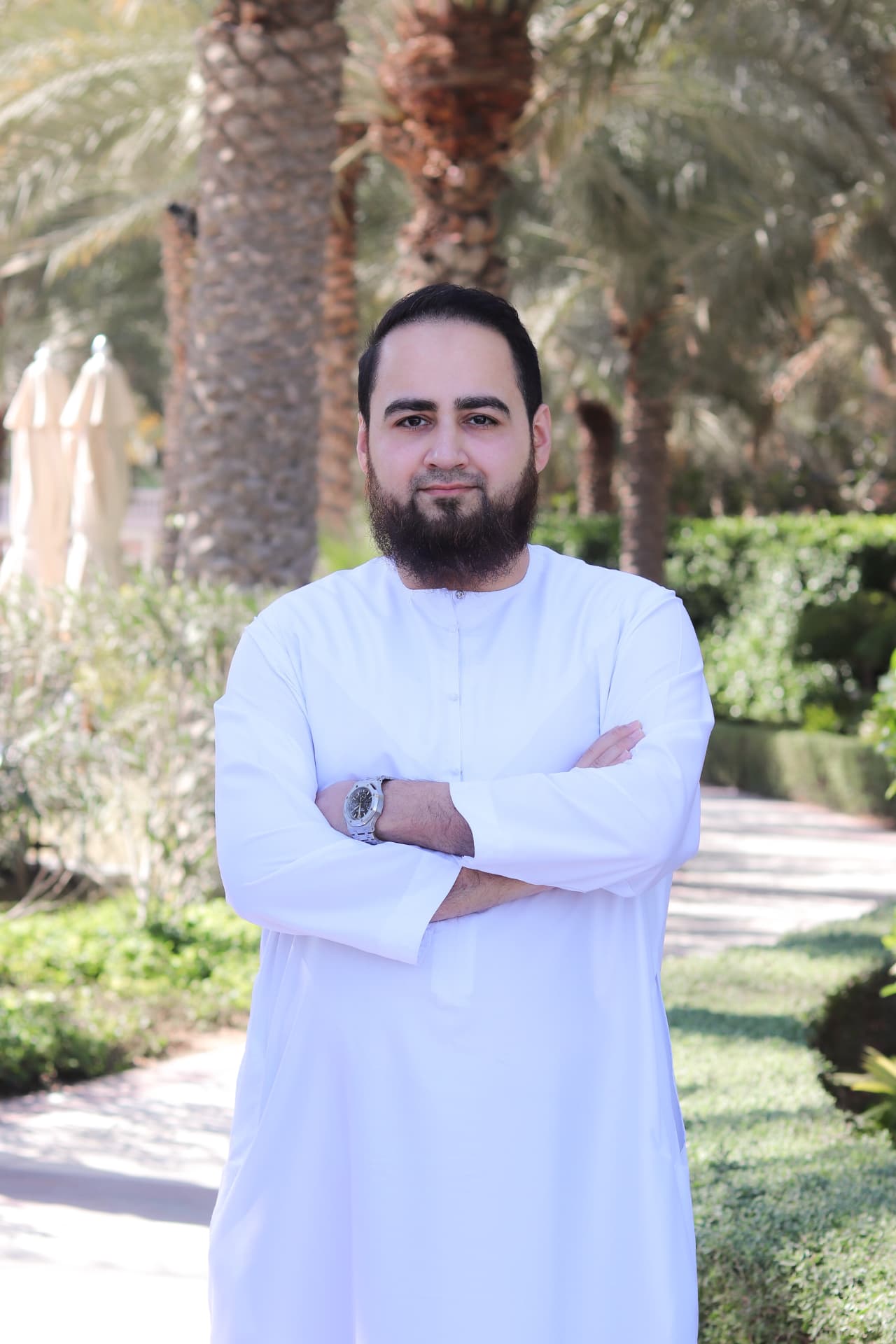 Huzefa Vorajee standing outdoors in Dubai, arms folded, wearing a white kandura